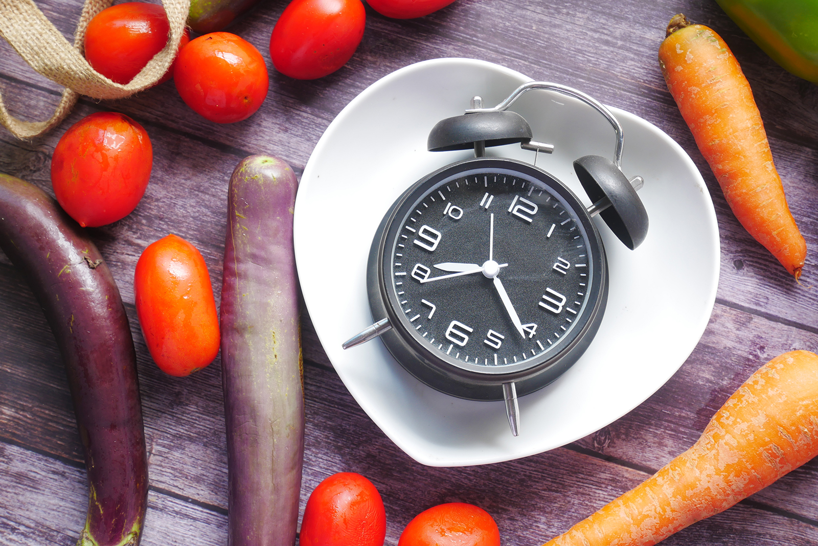 fresh vegetables and alarm clock on heart shape plate on table