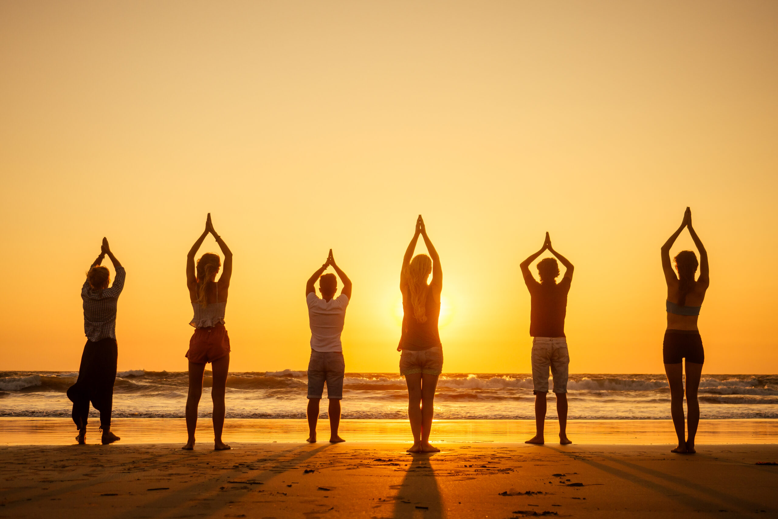 women doing yoga on beach at sunset